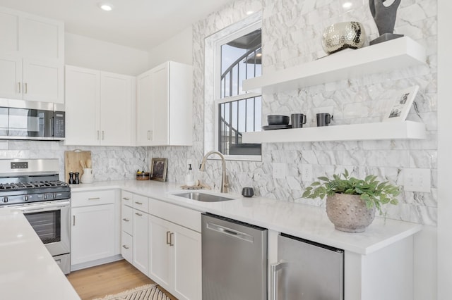 kitchen featuring appliances with stainless steel finishes, tasteful backsplash, white cabinetry, sink, and light wood-type flooring