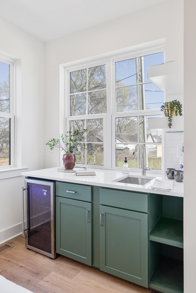 bar featuring wine cooler, green cabinetry, light hardwood / wood-style floors, and sink