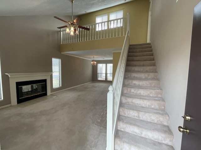 stairway with a towering ceiling, ceiling fan with notable chandelier, and carpet flooring