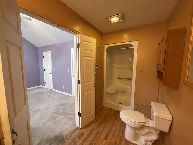 bathroom featuring walk in shower, wood-type flooring, toilet, and a textured ceiling