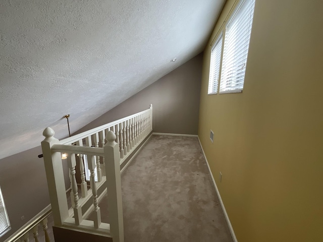 hallway featuring vaulted ceiling, carpet, and a textured ceiling