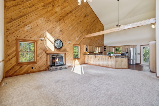 unfurnished living room featuring wood walls, ceiling fan, high vaulted ceiling, and a wealth of natural light