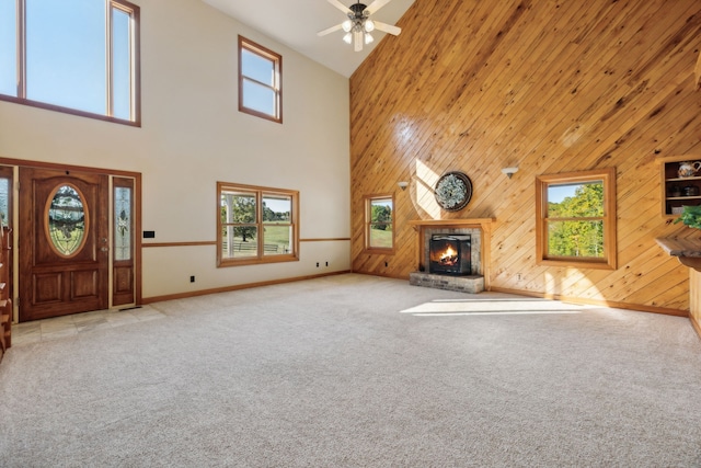 unfurnished living room with ceiling fan, light carpet, high vaulted ceiling, and wood walls