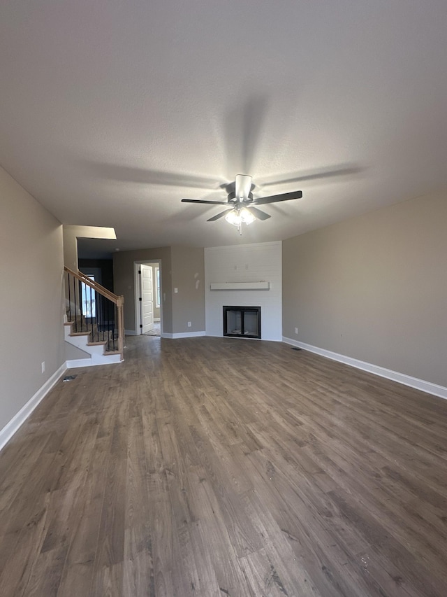 unfurnished living room with dark wood finished floors, a fireplace, baseboards, ceiling fan, and stairs