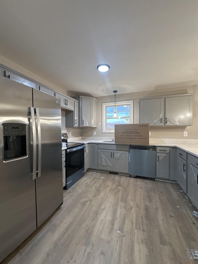 kitchen with pendant lighting, gray cabinets, wood finished floors, stainless steel appliances, and light countertops