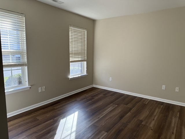 empty room with dark hardwood / wood-style floors and plenty of natural light