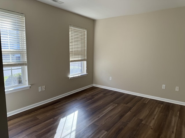 spare room featuring visible vents, dark wood-style flooring, baseboards, and a healthy amount of sunlight