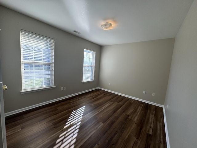 unfurnished room featuring visible vents, baseboards, and dark wood finished floors