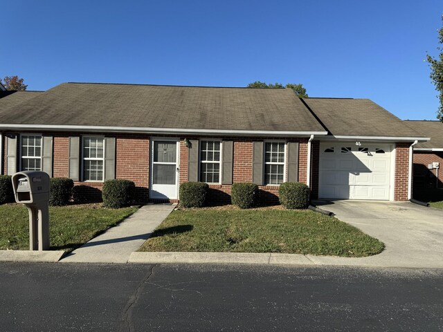 view of front of home featuring a front lawn, a garage, a shingled roof, driveway, and brick siding