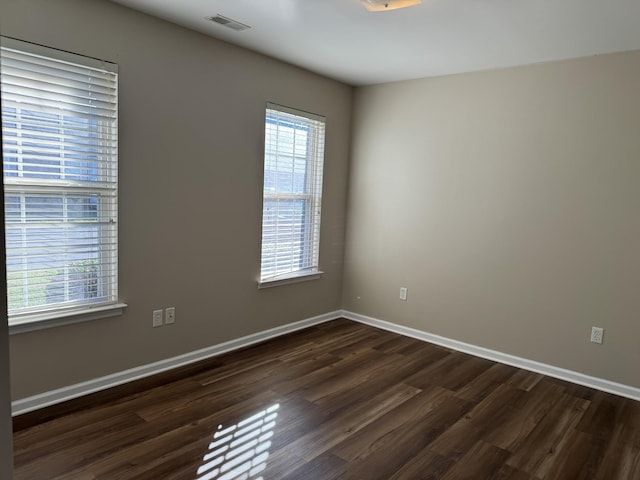 empty room featuring visible vents, baseboards, and dark wood finished floors