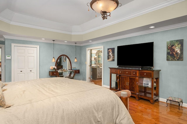 bedroom with a closet, crown molding, hardwood / wood-style flooring, and a raised ceiling