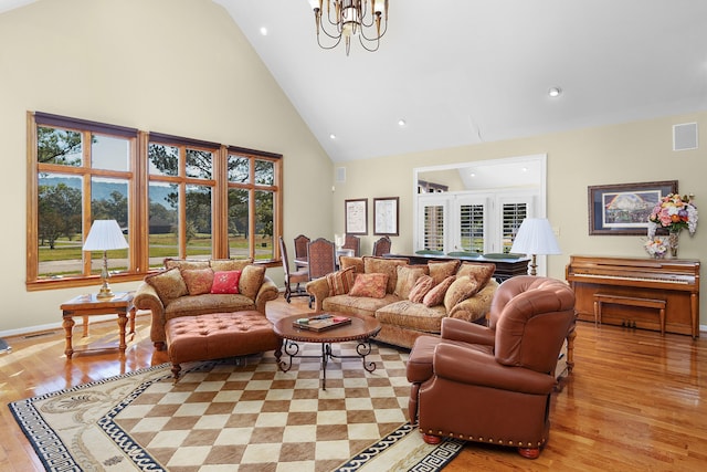 living room with a notable chandelier, high vaulted ceiling, a healthy amount of sunlight, and light hardwood / wood-style flooring