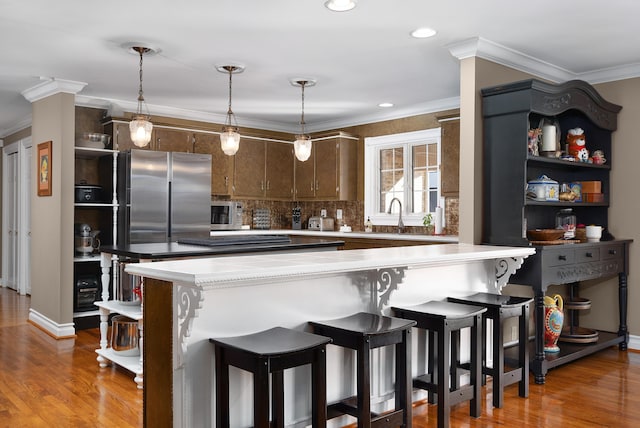 kitchen with kitchen peninsula, hardwood / wood-style floors, dark brown cabinets, a breakfast bar area, and crown molding