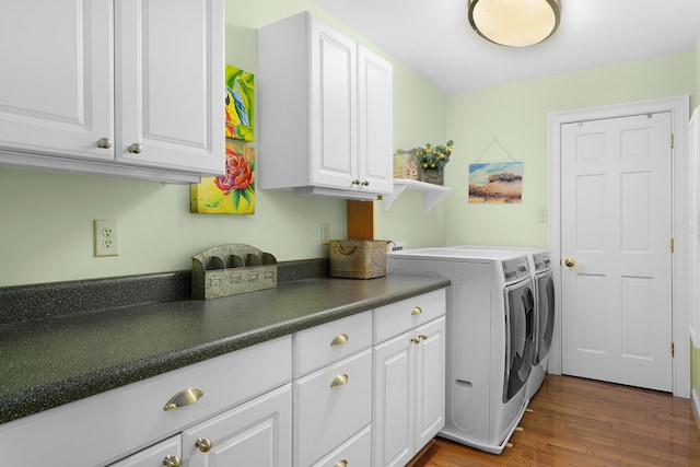 washroom featuring washing machine and dryer, wood-type flooring, and cabinets