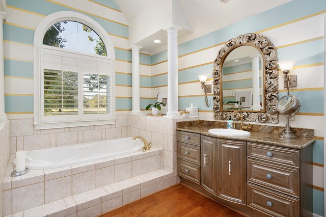 bathroom featuring ornate columns, tiled bath, wood-type flooring, vaulted ceiling, and vanity