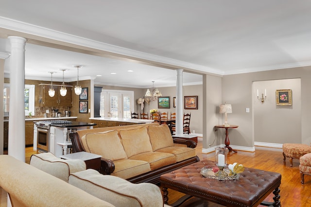 living room featuring ornate columns, crown molding, an inviting chandelier, and light wood-type flooring