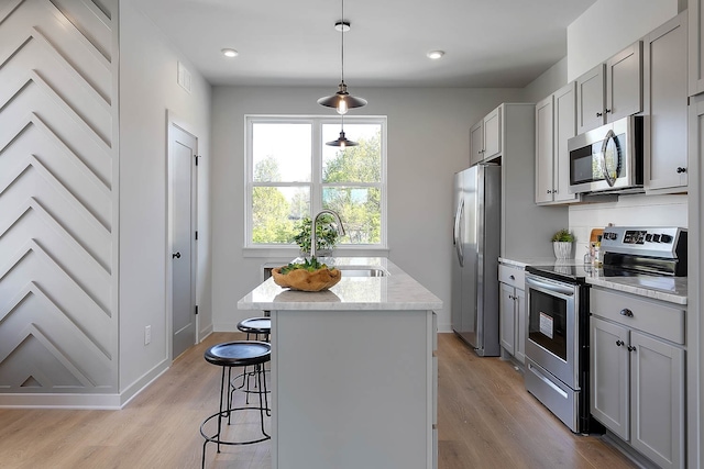 kitchen with appliances with stainless steel finishes, decorative light fixtures, light hardwood / wood-style flooring, and gray cabinetry