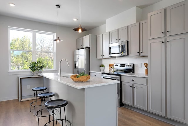 kitchen featuring sink, light stone counters, a center island with sink, appliances with stainless steel finishes, and gray cabinets