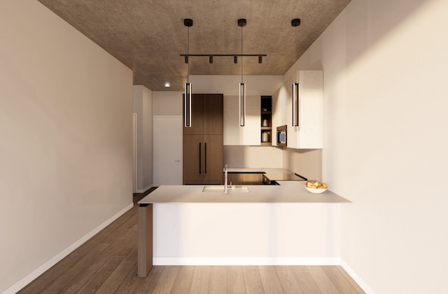 kitchen featuring sink, light wood-type flooring, kitchen peninsula, decorative light fixtures, and white cabinets