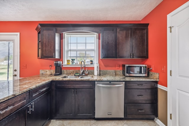 kitchen with sink, dark brown cabinets, light tile patterned floors, appliances with stainless steel finishes, and light stone countertops