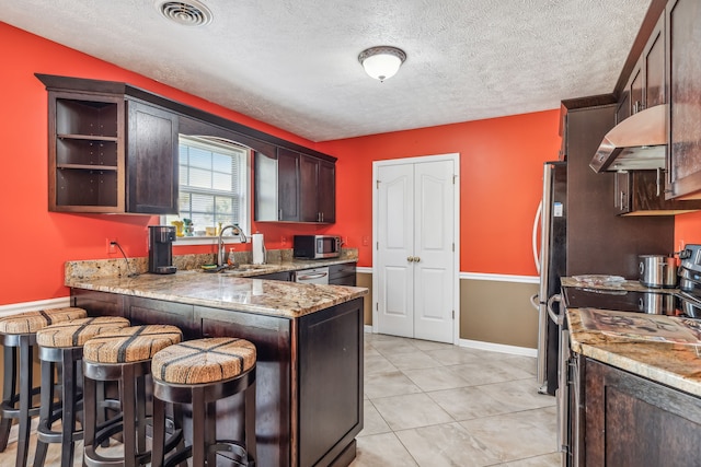 kitchen with sink, stainless steel appliances, light stone counters, ventilation hood, and kitchen peninsula