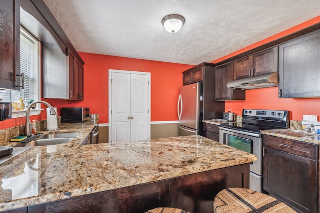 kitchen with appliances with stainless steel finishes, sink, light stone counters, kitchen peninsula, and a textured ceiling