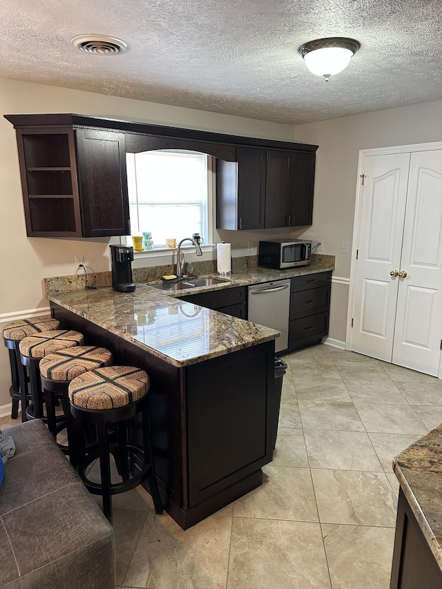 kitchen featuring appliances with stainless steel finishes, sink, light stone counters, kitchen peninsula, and dark brown cabinets