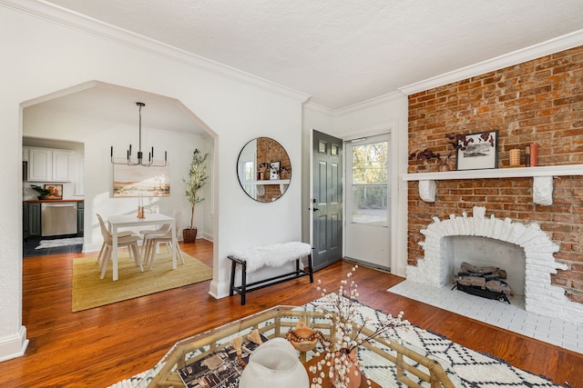 living room with hardwood / wood-style floors, a textured ceiling, a chandelier, a brick fireplace, and crown molding