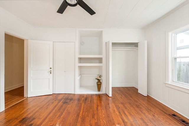 unfurnished bedroom with dark hardwood / wood-style floors, multiple closets, and ceiling fan