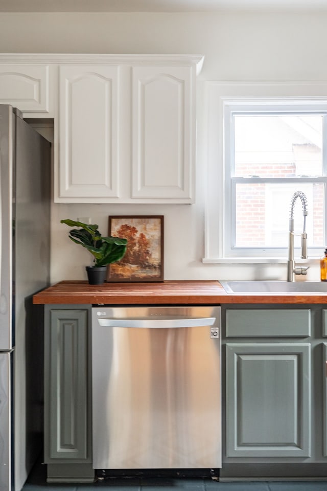 kitchen with butcher block countertops, sink, white cabinetry, and stainless steel appliances