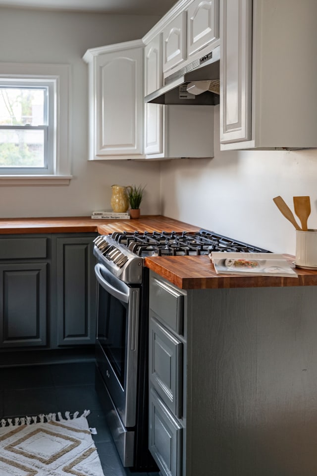 kitchen featuring white cabinets, dark tile patterned floors, gas range, butcher block counters, and gray cabinetry