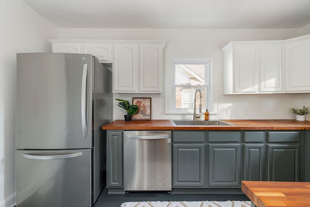 kitchen featuring wooden counters, dark tile patterned floors, stainless steel appliances, sink, and white cabinets