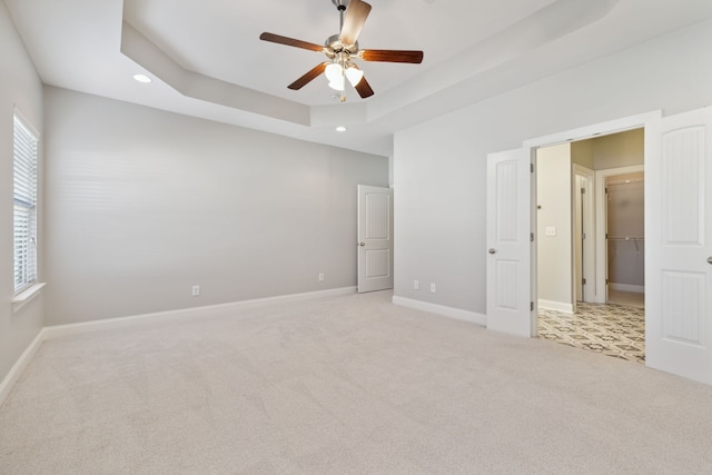 unfurnished bedroom featuring a closet, a walk in closet, a tray ceiling, light colored carpet, and ceiling fan