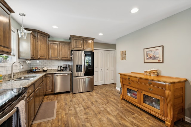 kitchen featuring light stone countertops, wood-type flooring, sink, stainless steel appliances, and pendant lighting