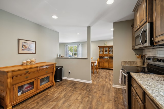 kitchen with appliances with stainless steel finishes, light stone counters, dark hardwood / wood-style floors, and backsplash