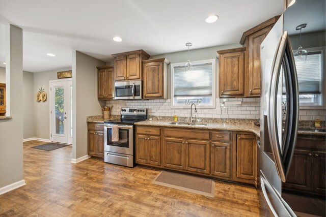 kitchen featuring backsplash, decorative light fixtures, appliances with stainless steel finishes, light stone counters, and dark hardwood / wood-style flooring