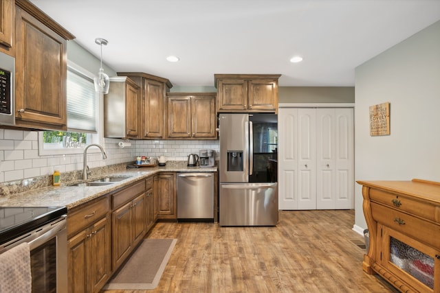 kitchen with tasteful backsplash, light wood-type flooring, sink, pendant lighting, and stainless steel appliances