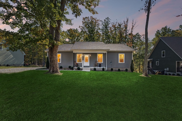 back house at dusk featuring covered porch and a lawn