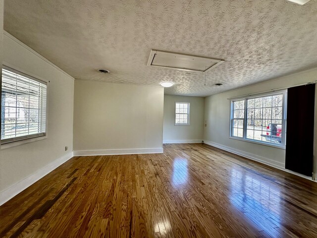 empty room featuring visible vents, a textured ceiling, wood finished floors, and attic access