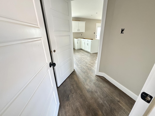 hallway featuring baseboards and dark wood-type flooring