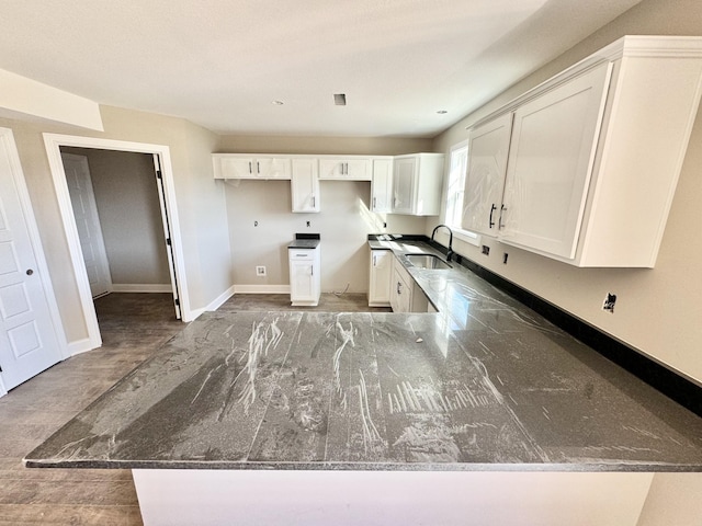 kitchen with white cabinetry, kitchen peninsula, sink, and dark stone countertops