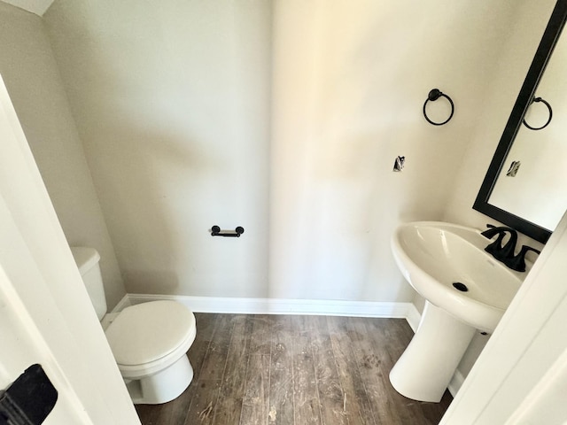 half bath with toilet, baseboards, and wood finished floors