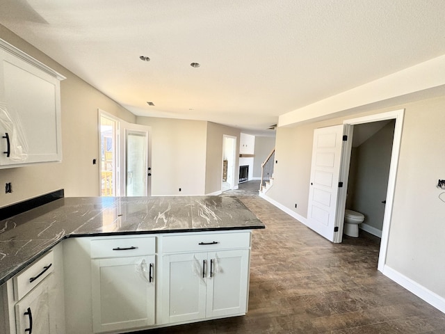 kitchen featuring dark stone countertops, dark hardwood / wood-style floors, kitchen peninsula, and white cabinets