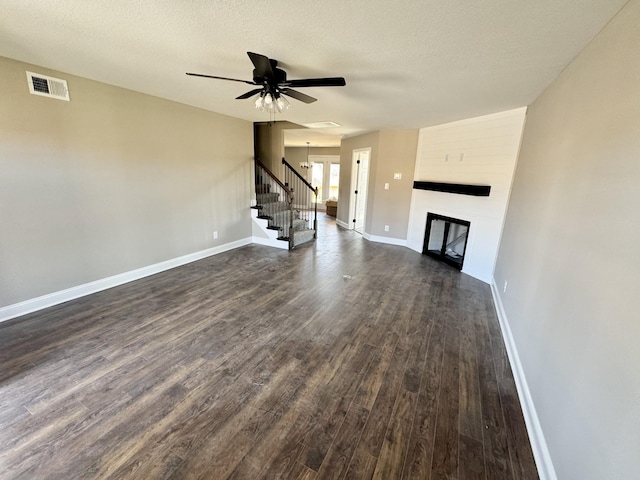 unfurnished living room featuring visible vents, dark wood-style floors, a fireplace, and stairs