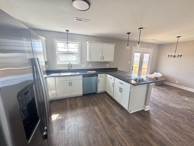 kitchen featuring dark countertops, dark wood finished floors, a peninsula, stainless steel appliances, and a sink