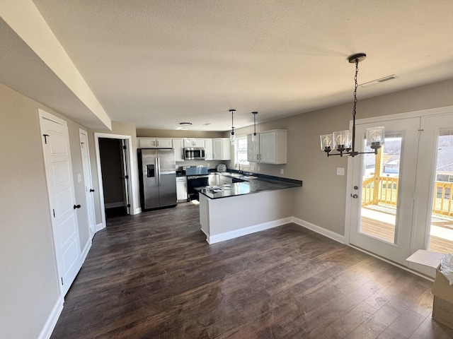 kitchen with dark wood finished floors, white cabinetry, an inviting chandelier, appliances with stainless steel finishes, and a peninsula