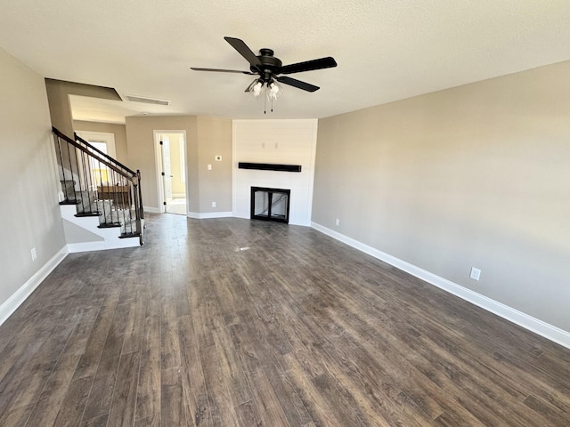 unfurnished living room with visible vents, a large fireplace, dark wood-type flooring, baseboards, and stairway