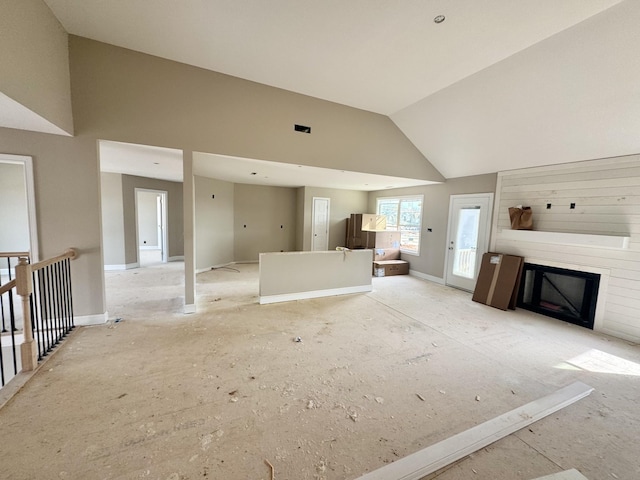 unfurnished living room with baseboards, high vaulted ceiling, and a fireplace