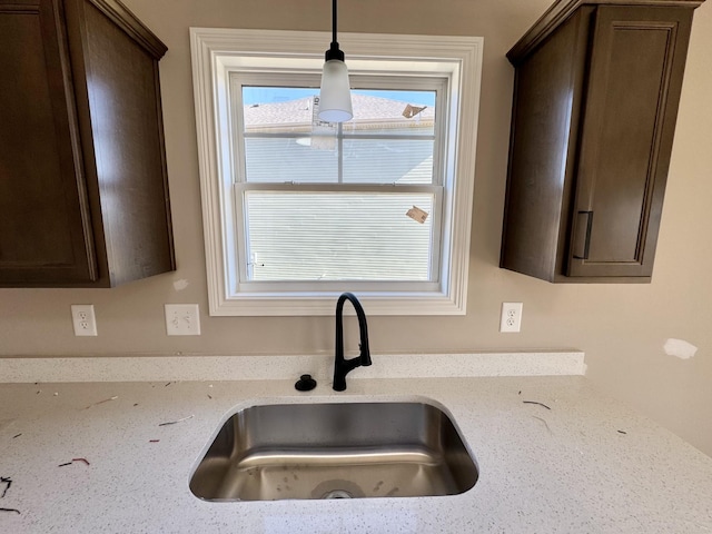 kitchen featuring light stone countertops, sink, dark brown cabinets, and decorative light fixtures