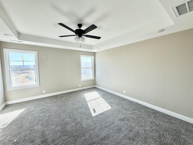 spare room with a raised ceiling, ceiling fan, and dark carpet